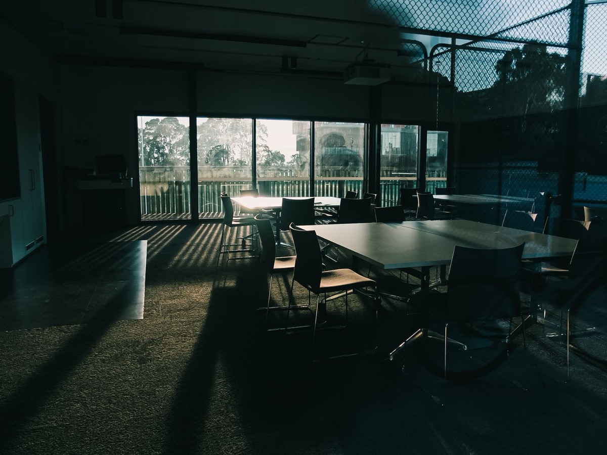 A meeting room with tables and chairs and large windows letting in low sunlight