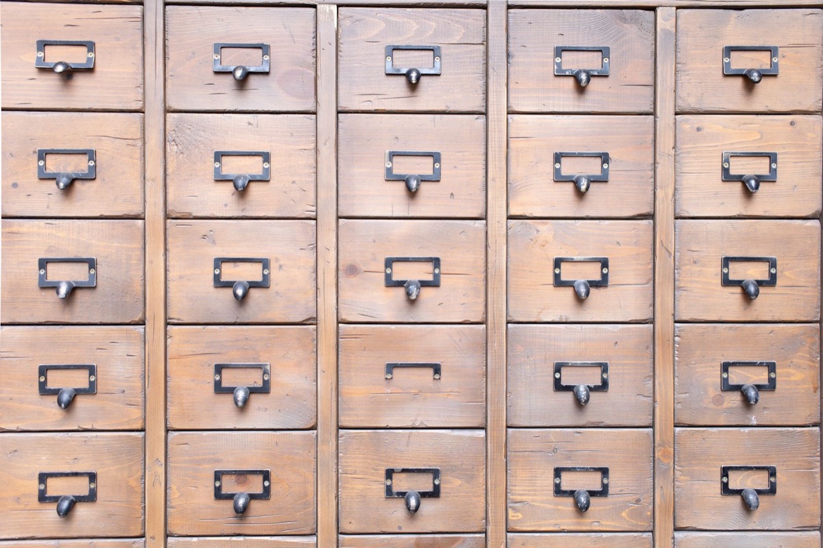 A wall of aged wooden archive drawers with metal handles and empty label holders