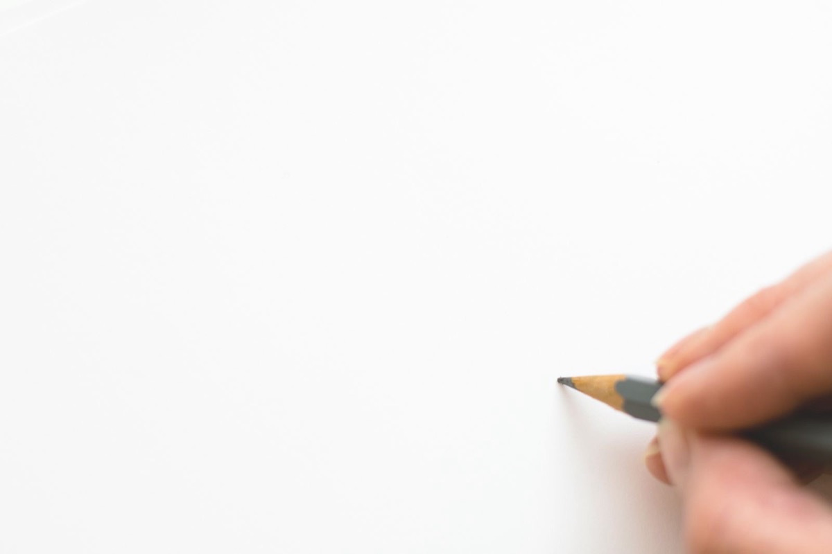 A hand holding a sharpened pencil above a clean blank white sheet of paper