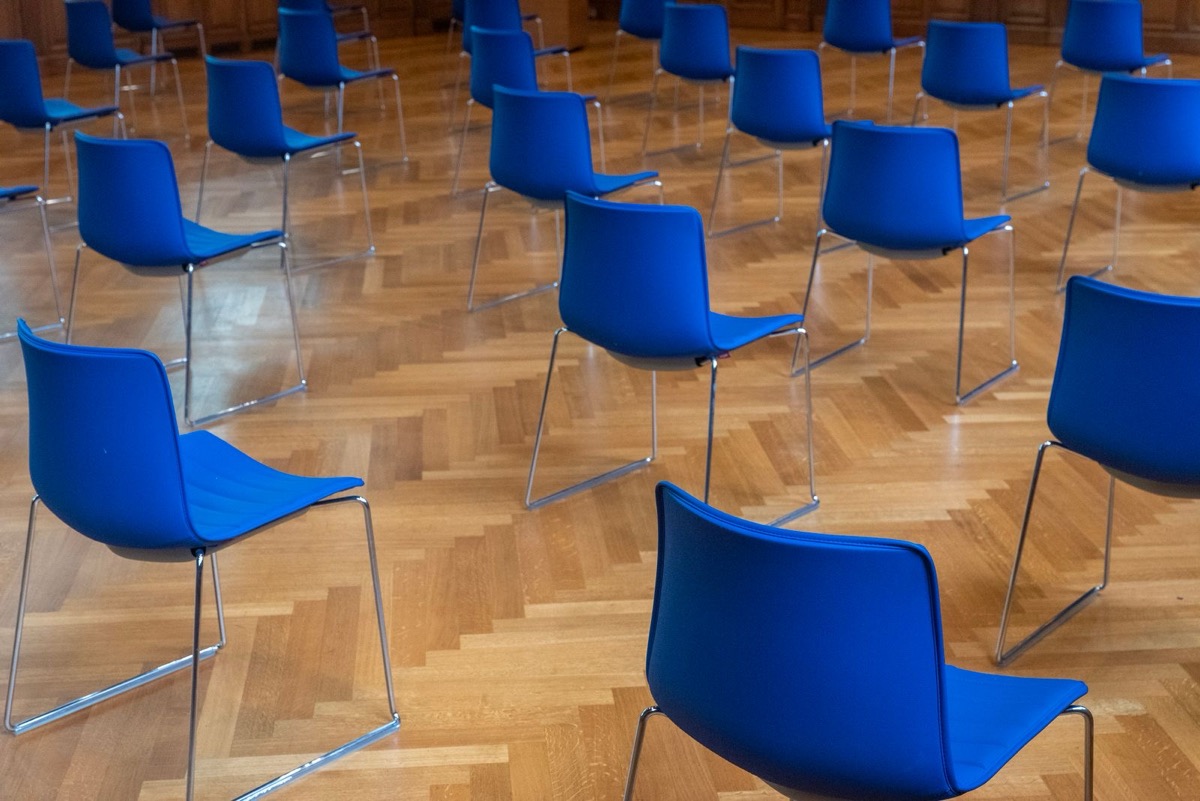 Rows of empty blue chairs on a polished parquet floor in a large room