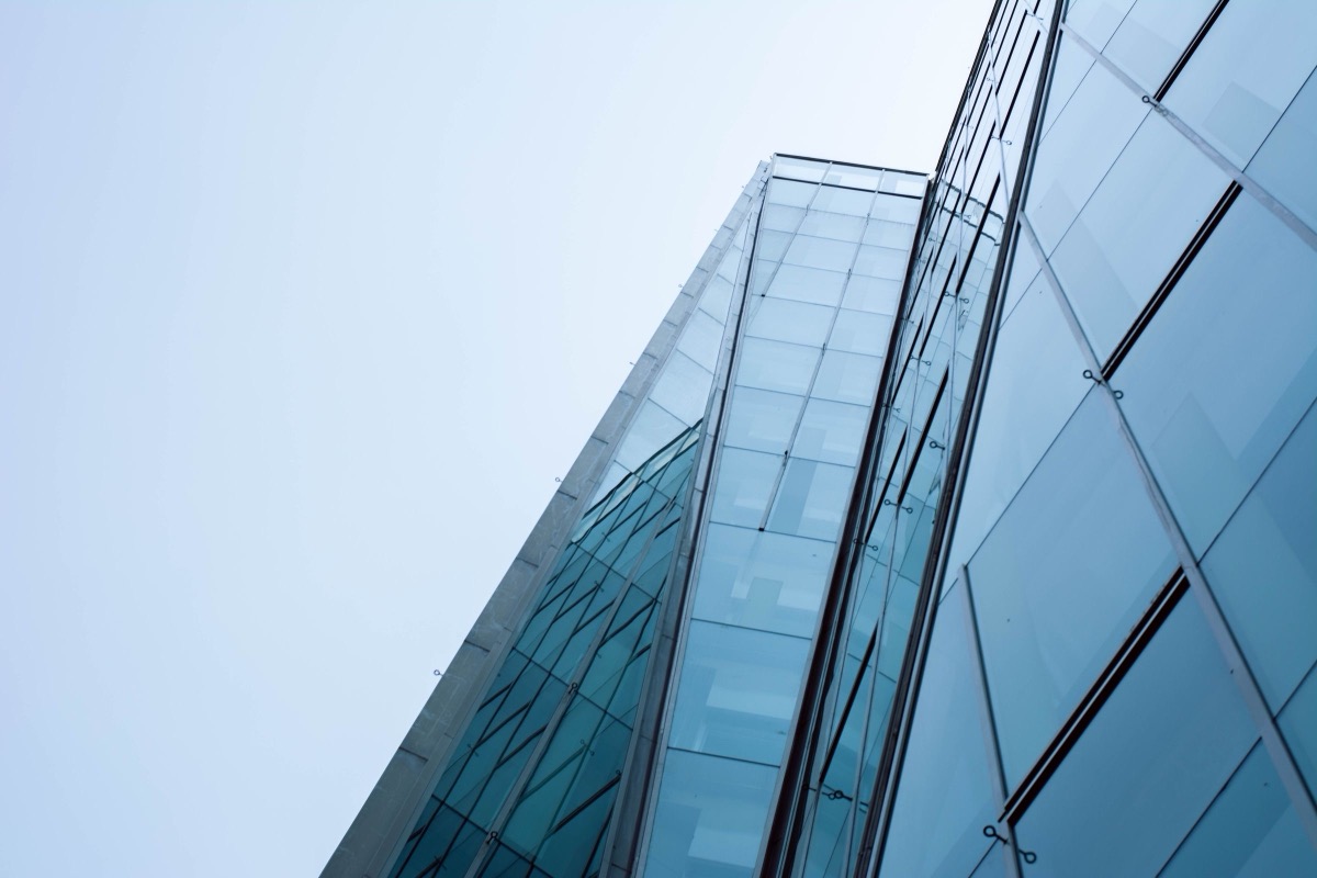 Looking up at the glass facade of a modern office building against a pale, hazy sky