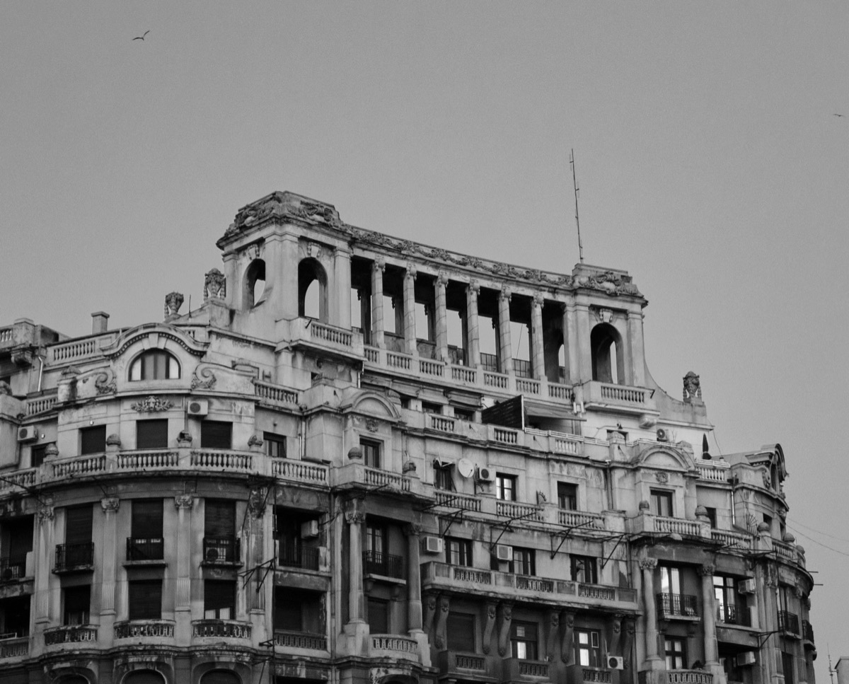Black and white view of an ornate apartment building with balconies, columns and an open rooftop loggia