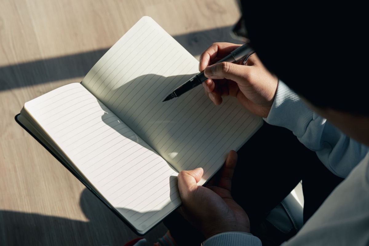 Hands holding a fountain pen over an open blank lined notebook in warm sunlight