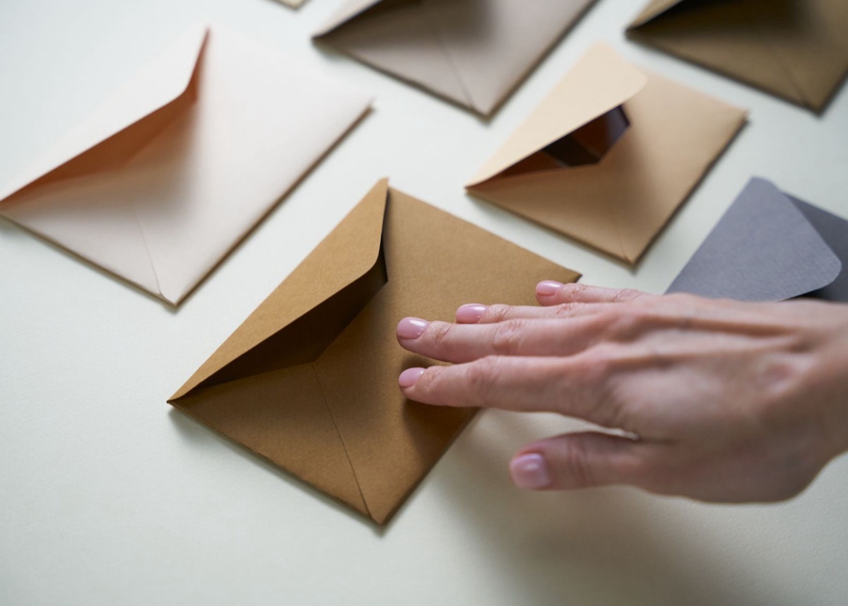 A hand resting on plain envelopes in different colours laid out on a pale surface