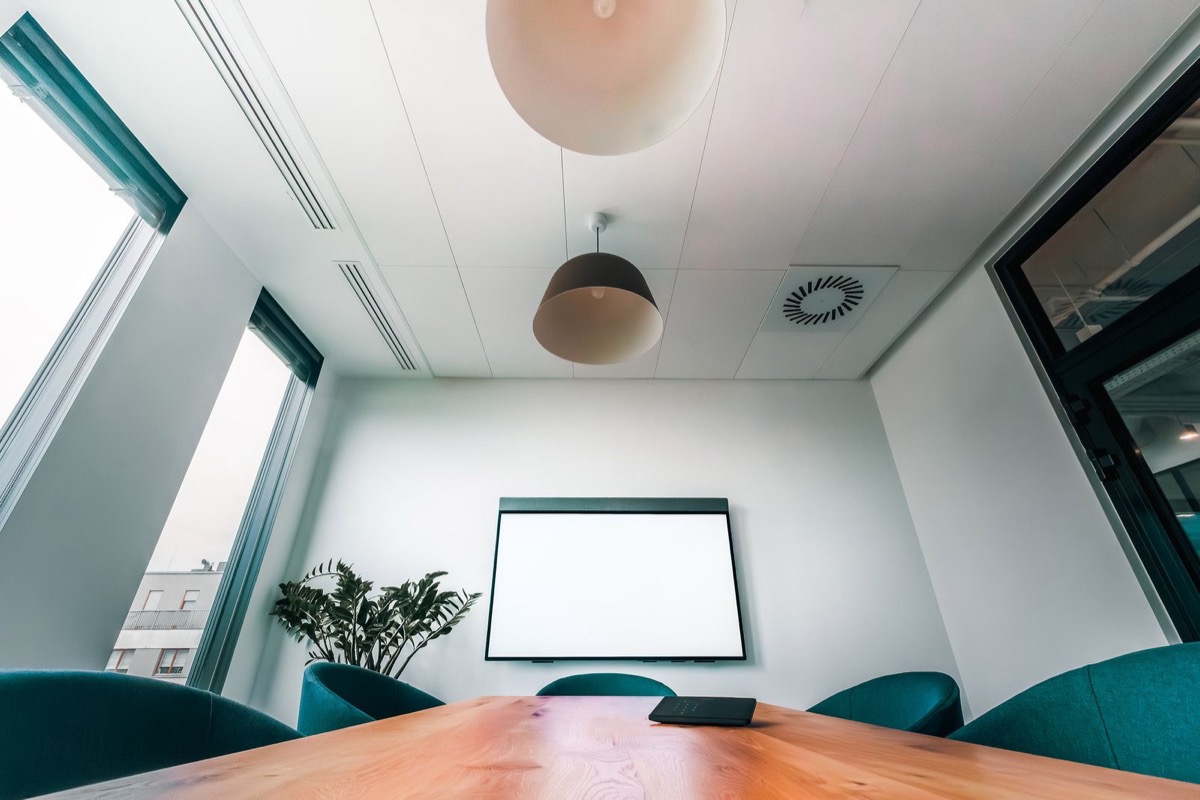 An empty meeting room with a wooden table, teal chairs and a blank wall screen