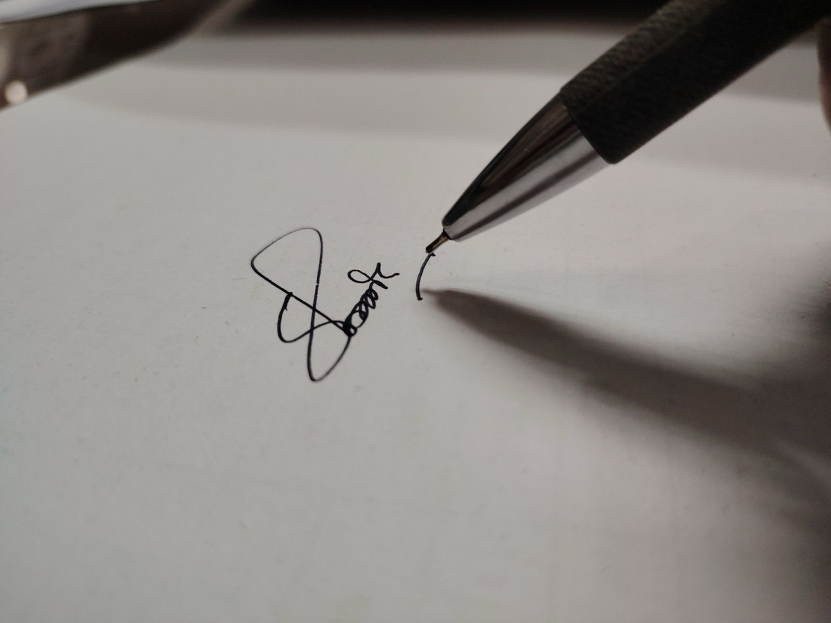 Close-up of a pen finishing a handwritten signature on a sheet of white paper