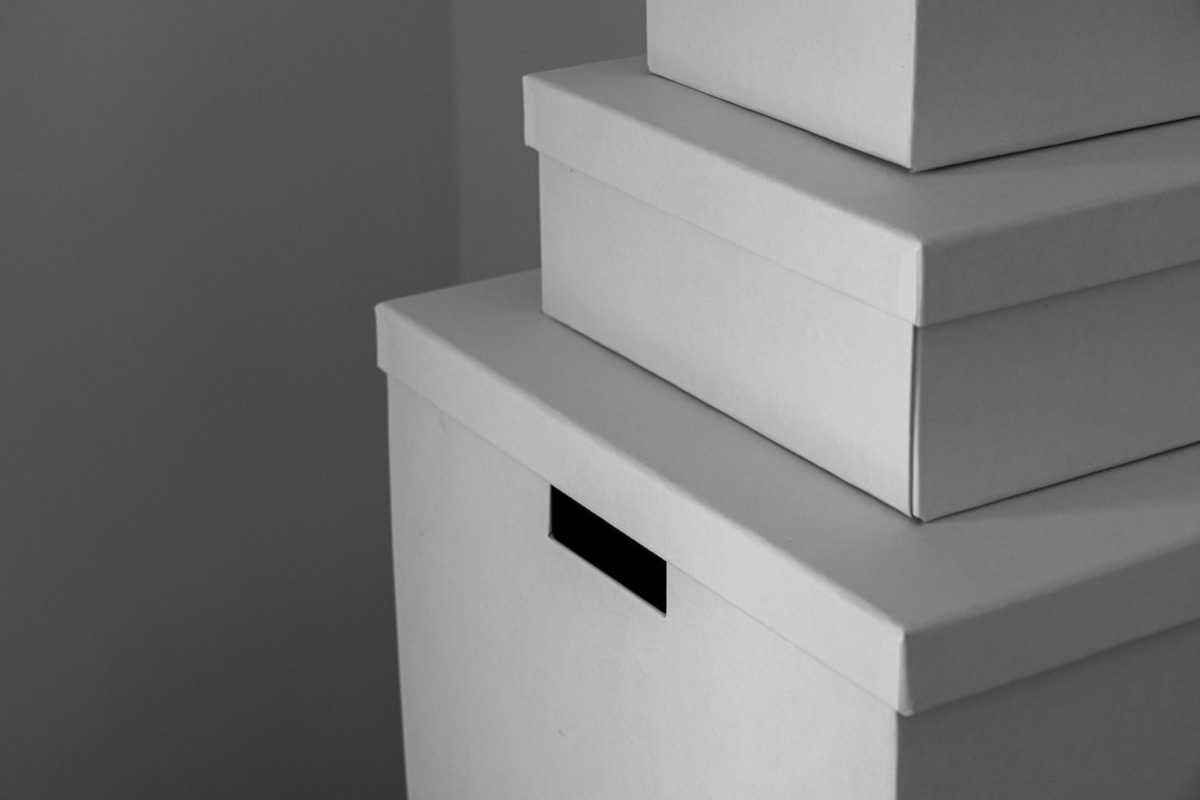 Stacked pale storage boxes with lids against a grey wall, the largest with a handle slot