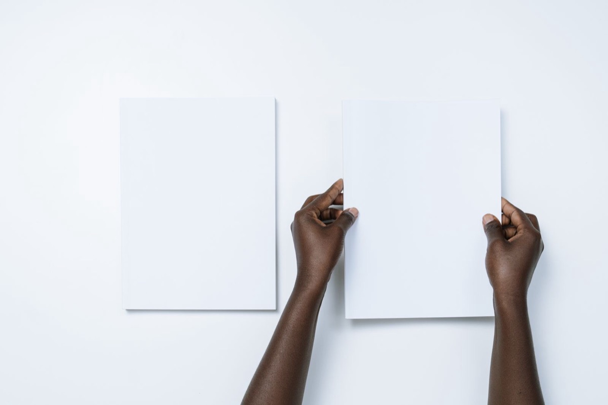 Two hands holding a blank white sheet beside a second blank sheet on a plain white surface