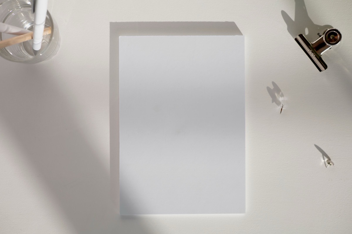 A blank sheet of paper on a white desk, with a glass pen holder and a metal binder clip