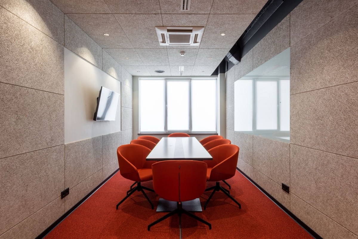 An empty meeting room with a long table, orange chairs and a wall-mounted screen